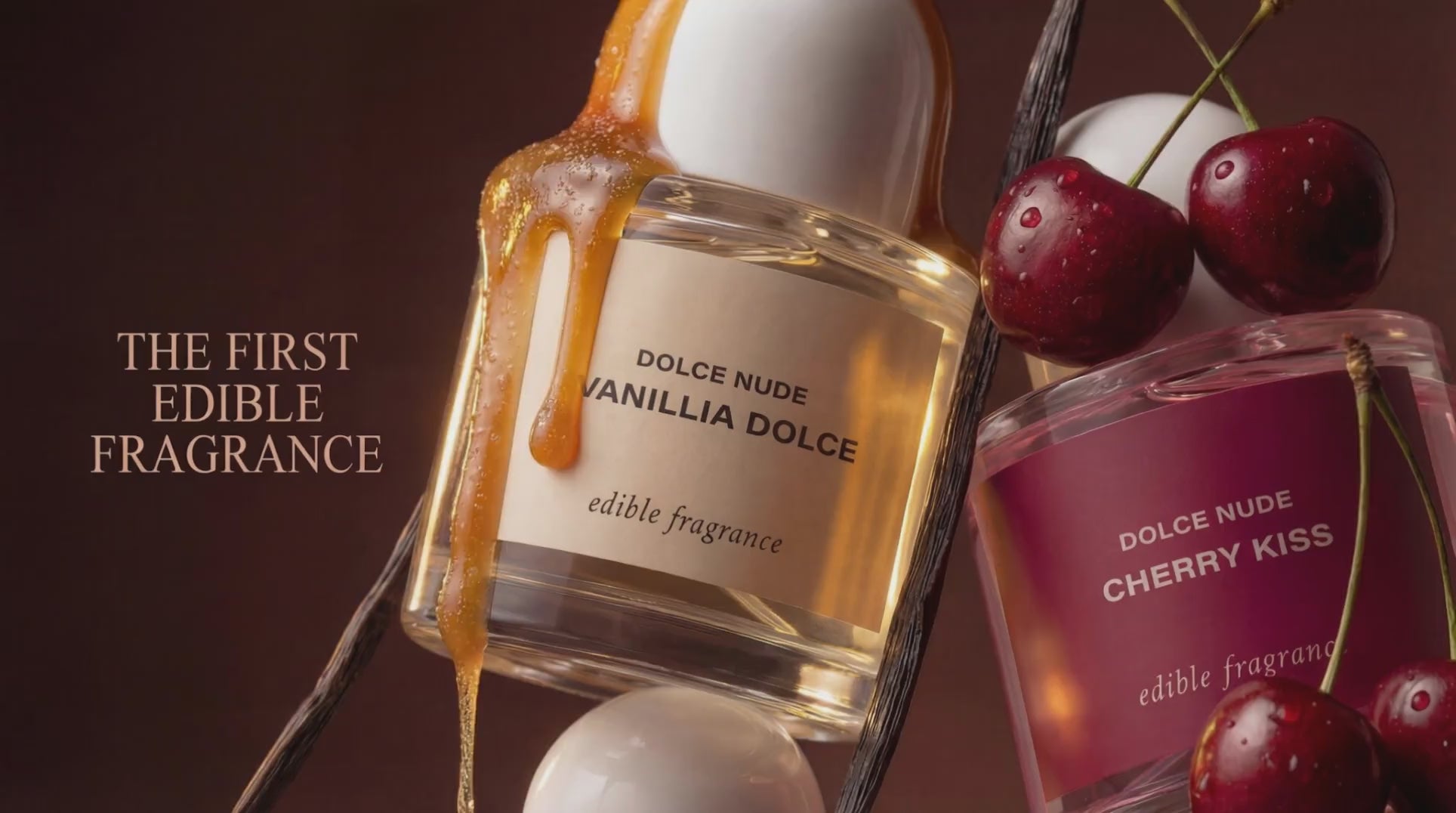 Load video: DOLCE NUDE Vanillia Dolce and Cherry Kiss edible fragrances displayed with fresh cherries and golden honey drip, text reads the first edible fragrance